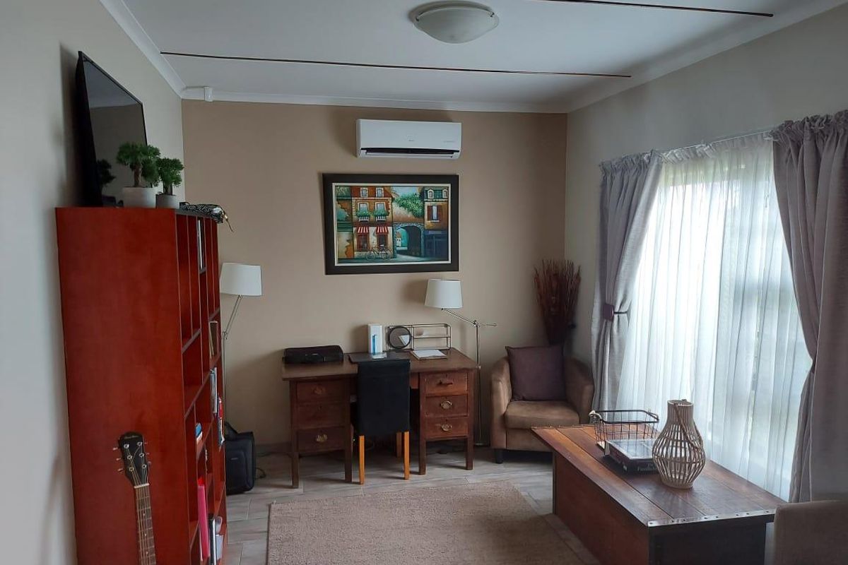 A functional living area featuring a wall-mounted air conditioning unit, tiled flooring, and large windows with curtains allowing for natural light.