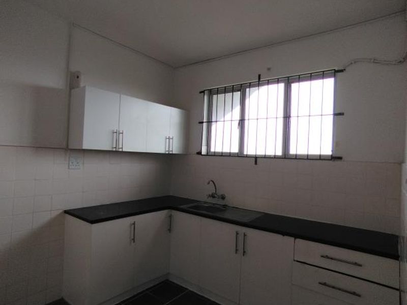 A functional kitchen featuring white cabinetry, dark countertops, tiled backsplash, and tiled flooring, equipped with a stainless steel sink and security window bars.