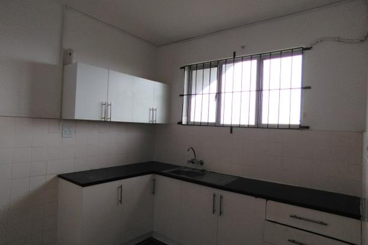A functional kitchen featuring white cabinetry, dark countertops, tiled backsplash, and tiled flooring, equipped with a stainless steel sink and security window bars.