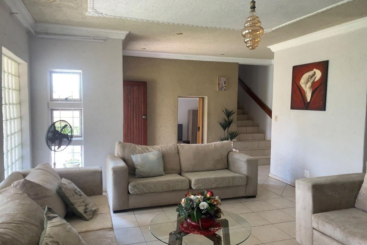 Spacious living room featuring tiled flooring, ornate ceiling cornices, a central ceiling rose, and a staircase leading to the upper level.