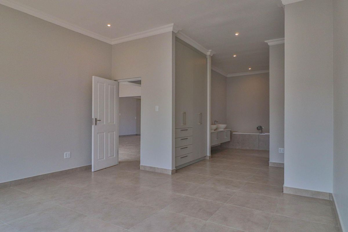 A spacious bedroom featuring neutral tiled flooring, recessed ceiling lighting, built-in cabinetry, and an open-plan en-suite bathroom area.