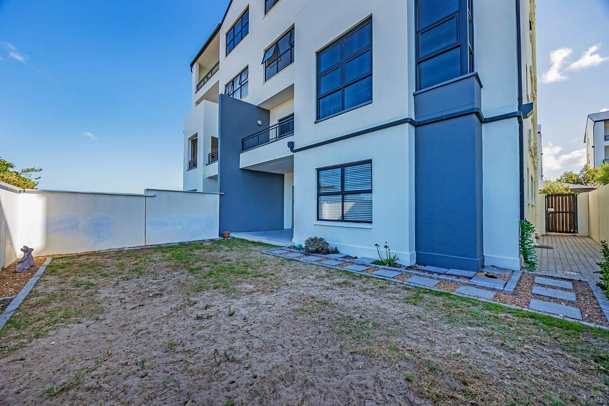 Rear view of the apartment building featuring a private garden area, paved walkway, and access to upper-level balconies.