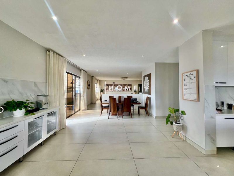 Spacious open-plan living and dining area featuring modern tiled flooring, recessed lighting, and seamless access to the outdoor patio through large sliding glass doors.