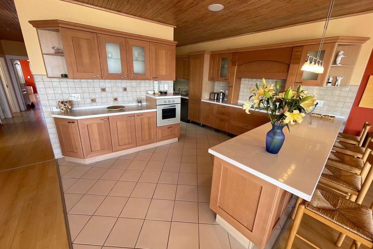 Spacious kitchen featuring wooden cabinetry, tiled flooring, a central island with stone countertop, and a warm timber-paneled ceiling.