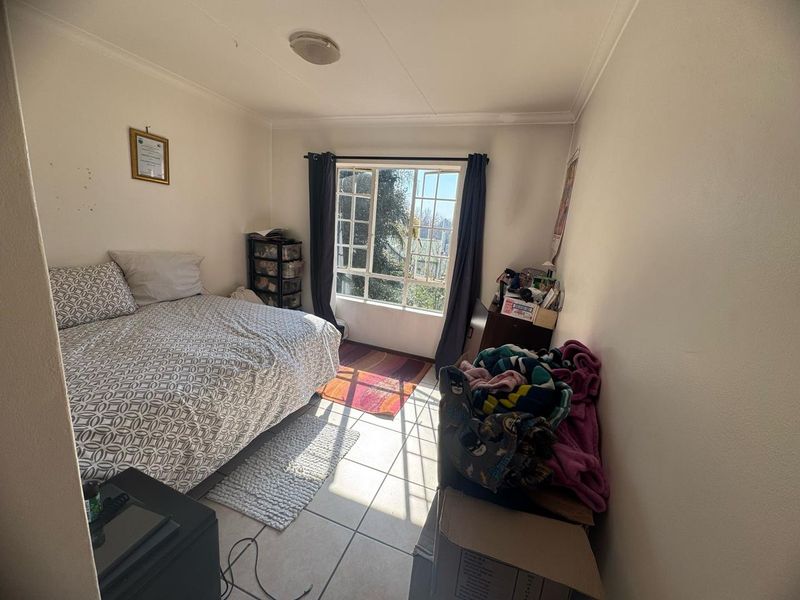 A functional bedroom featuring tiled flooring and a large window that provides natural light, offering a blank canvas for potential interior updates.