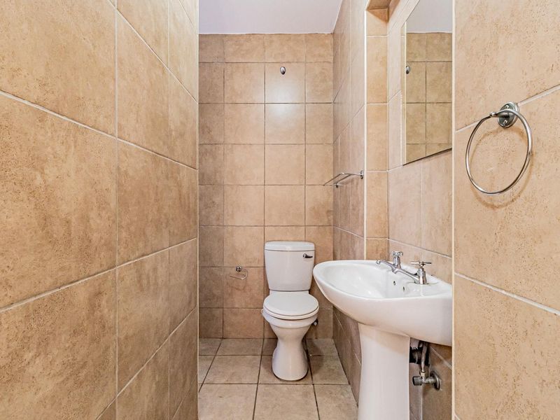 A compact bathroom featuring full-height beige wall tiling, a pedestal basin, and a standard toilet, presenting a clean and functional space.