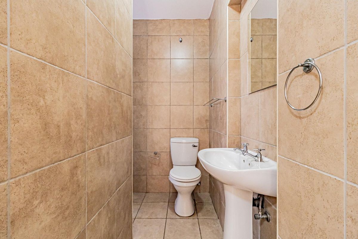 A compact bathroom featuring full-height beige wall tiling, a pedestal basin, and a standard toilet, presenting a clean and functional space.