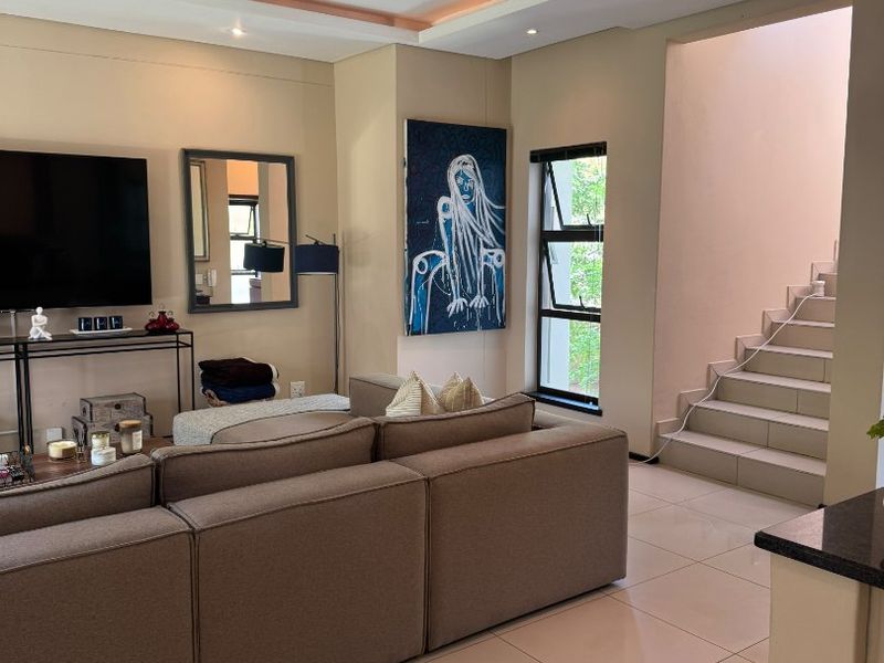 A well-maintained living room featuring tiled floors, recessed ceiling lighting, and an integrated staircase leading to the upper level.