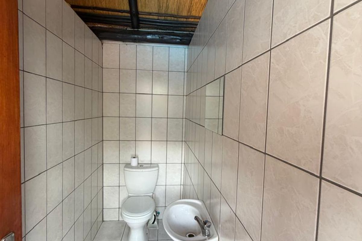 A compact bathroom featuring floor-to-ceiling wall tiles, a wall-mounted basin, a toilet, and a traditional exposed thatched roof ceiling.