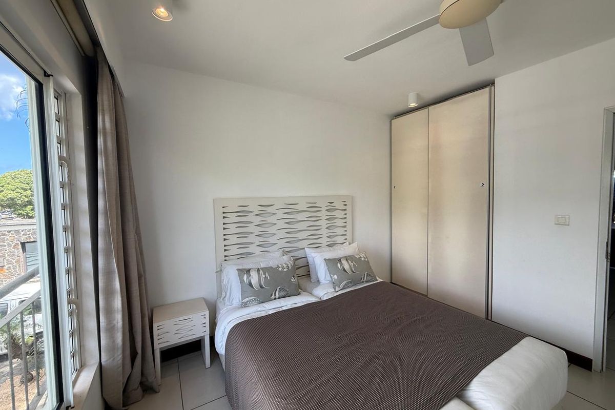A bright bedroom featuring built-in wardrobes, a ceiling fan, and large windows providing natural light and access to an outdoor balcony area.