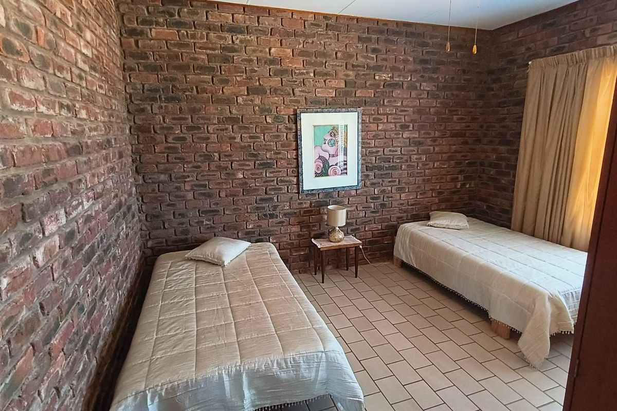 A bedroom featuring exposed brick walls and tiled flooring, providing a rustic aesthetic with natural light from the window.