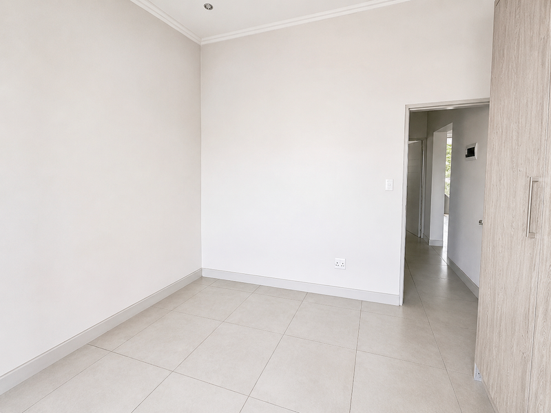 A bright, empty bedroom featuring neutral tiled flooring, built-in wardrobe cabinetry, and clean white walls, offering a versatile space ready for personalization.