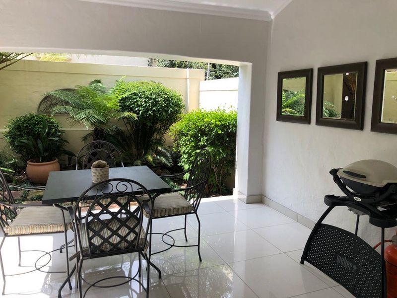 A covered patio area featuring tiled flooring and direct access to a private garden space, ideal for outdoor dining and relaxation.