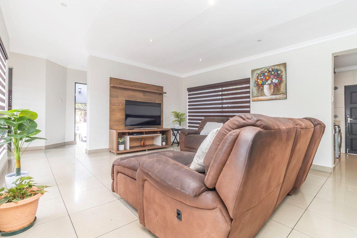 A bright and spacious living room featuring neutral tiled flooring, recessed ceiling lighting, and a modern built-in media wall unit.