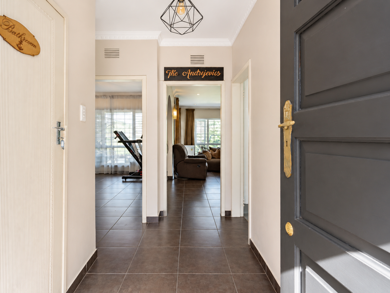 A bright and welcoming entrance hallway featuring tiled flooring, decorative cornice, and a modern pendant light, providing access to the main living areas.