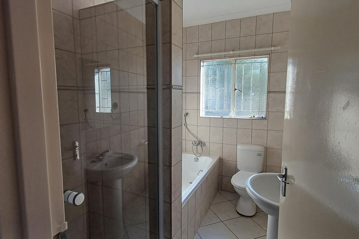 A functional bathroom featuring a tiled shower enclosure, a built-in bathtub, a pedestal basin, and a toilet with a window for natural ventilation.