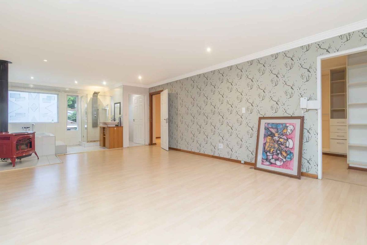 Spacious bedroom featuring light wood-look flooring, patterned wallpaper, an integrated fireplace, and an open-plan en-suite bathroom with a walk-in closet.