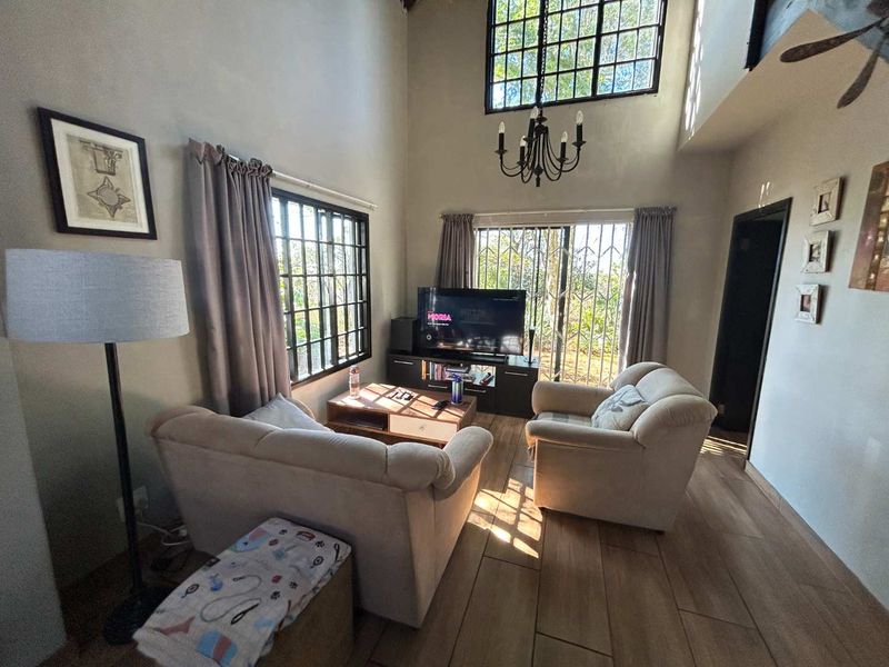 Spacious double-volume living room featuring wood-look tile flooring, a large feature window, and a wrought iron chandelier, offering abundant natural light.