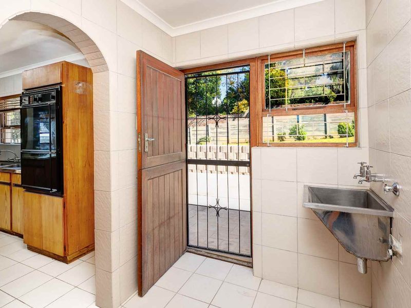 A functional laundry area featuring a stainless steel utility sink, tiled surfaces, and direct access to the exterior via a secure timber door.