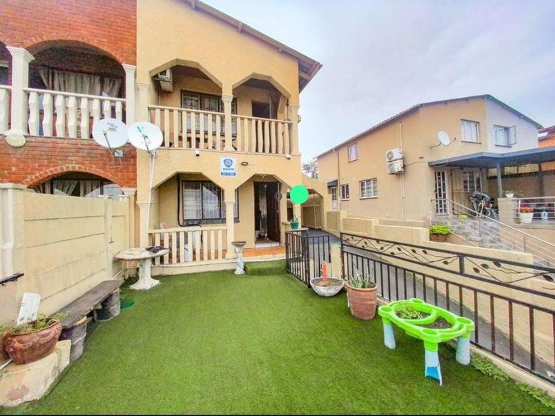 Rear exterior view of a two-story residential property featuring a small artificial lawn area, a balcony, and security features including bars and gates.