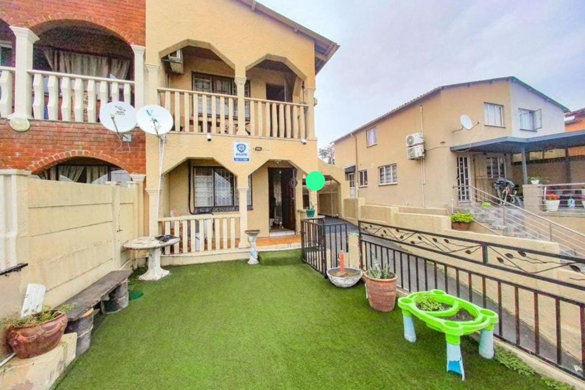 Rear exterior view of a two-story residential property featuring a small artificial lawn area, a balcony, and security features including bars and gates.