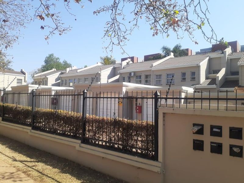 Front exterior view of a townhouse complex featuring tiled roofs, garage access, and secure perimeter fencing with integrated post boxes.