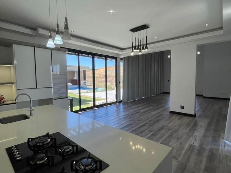 Modern open-plan kitchen and living area featuring a central island with gas hob, sleek cabinetry, and large sliding doors opening to the outdoor space.