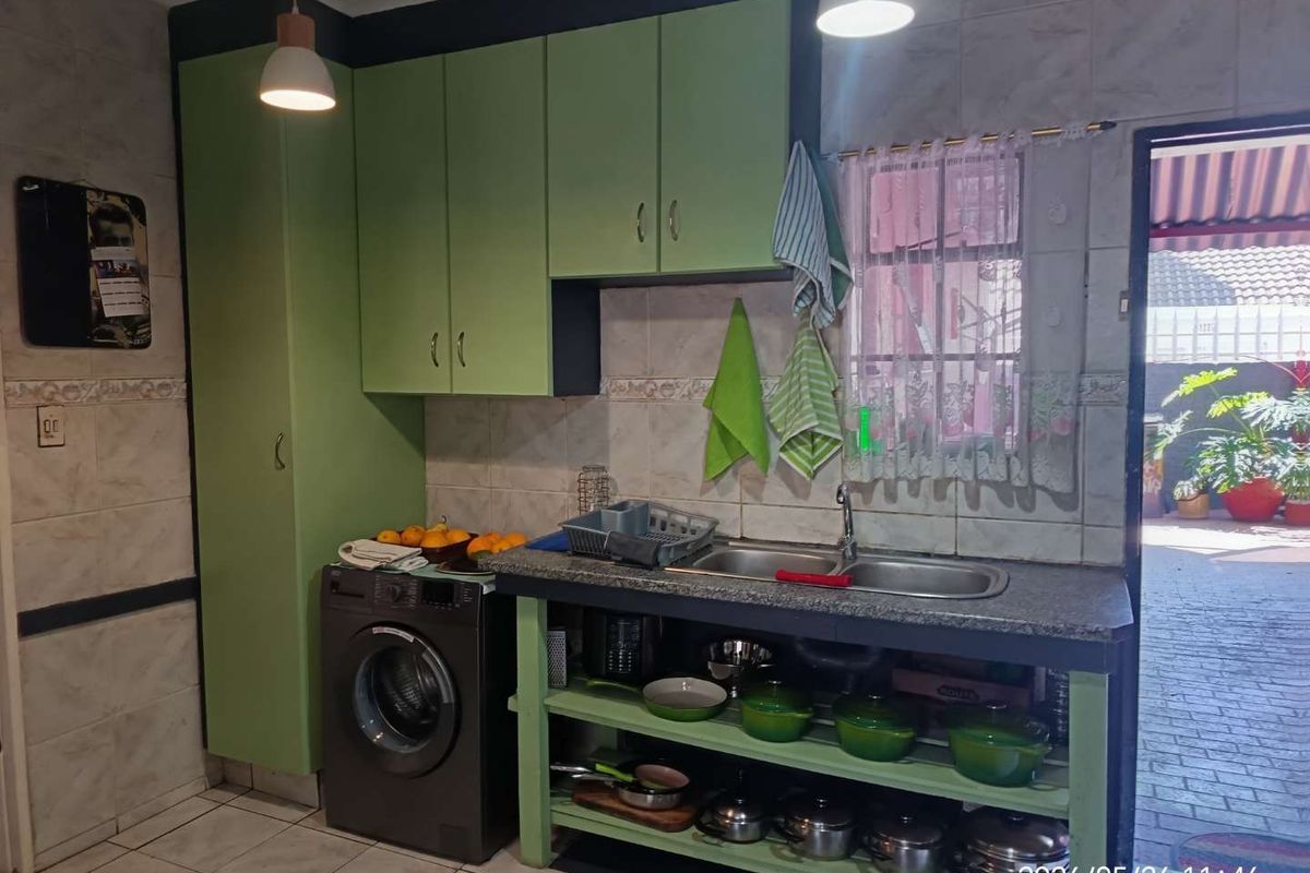 A functional kitchen area featuring green cabinetry, a double basin sink, tiled splashbacks, and space for a front-loading washing machine.