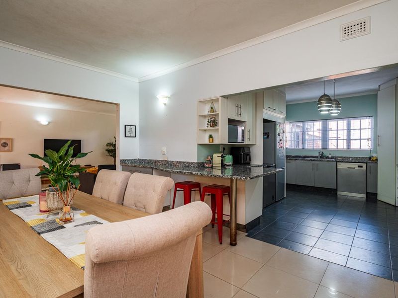 Open-plan living and dining area featuring a functional kitchen with granite countertops, breakfast bar, and tiled flooring, creating a cohesive and practical living space.