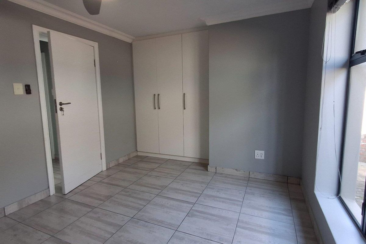 A clean, empty bedroom featuring neutral grey walls, light-toned tiled flooring, and built-in white cupboards with modern handles.
