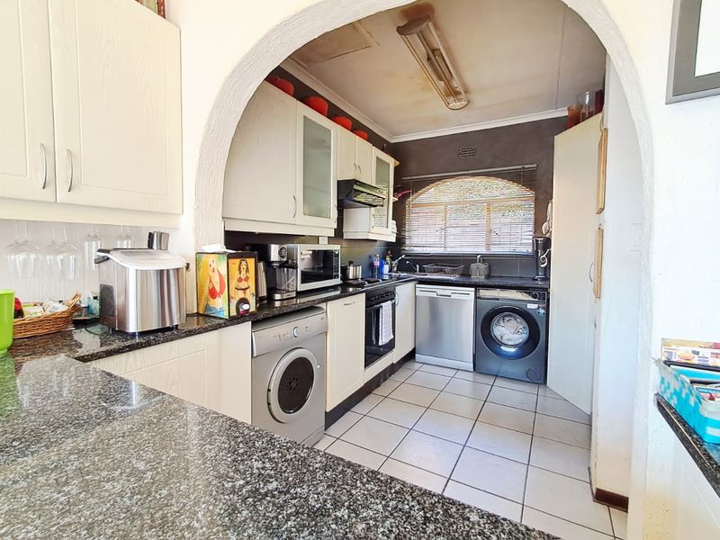 Compact kitchen featuring granite countertops, built-in cabinetry, and integrated appliances, accessed through a characterful arched doorway.