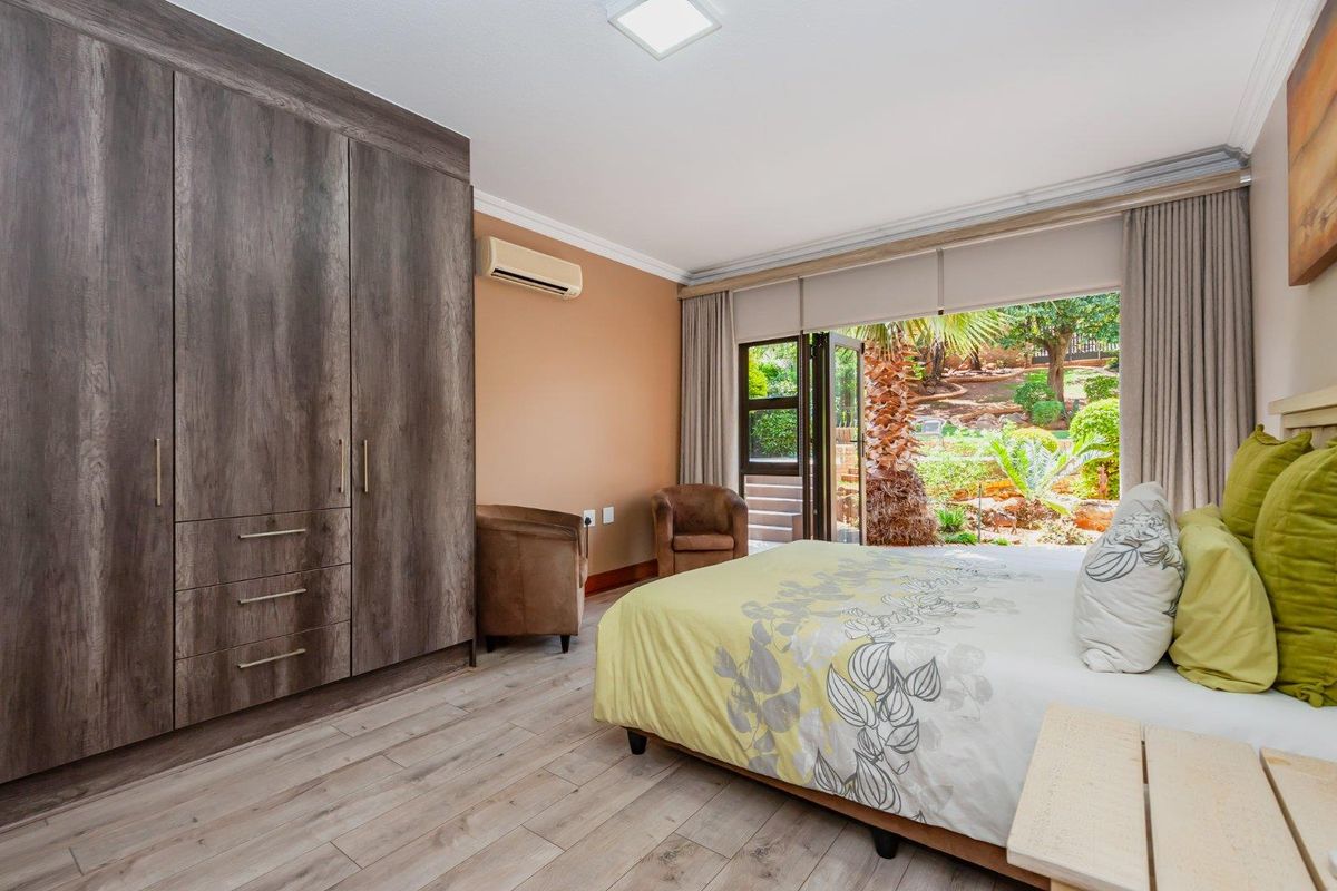 Spacious bedroom featuring built-in wooden cabinetry, air conditioning unit, and large glass doors opening directly onto a landscaped garden.