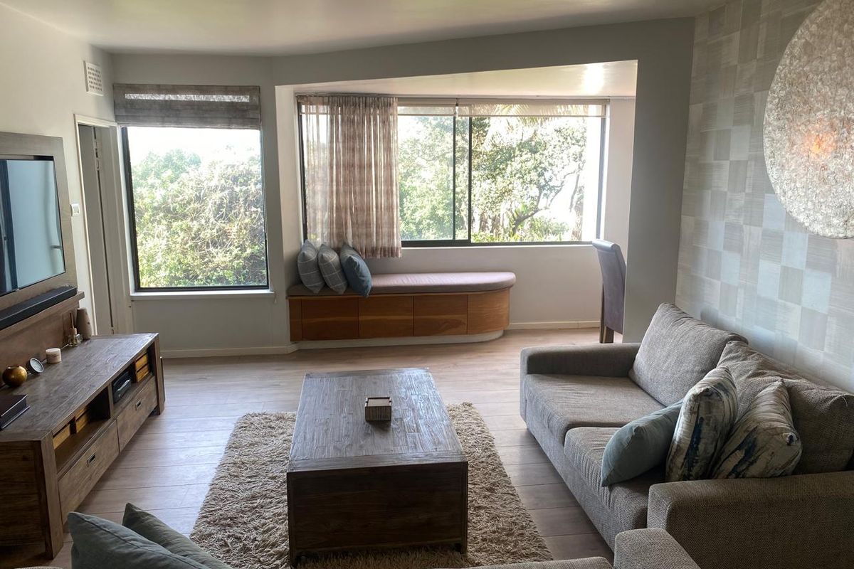 A bright and comfortable living room featuring a custom built-in window seat, large sliding windows, and modern laminate flooring.