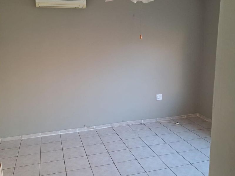 An empty bedroom featuring ceramic tiled flooring, a ceiling fan, and a wall-mounted split-system air conditioning unit.