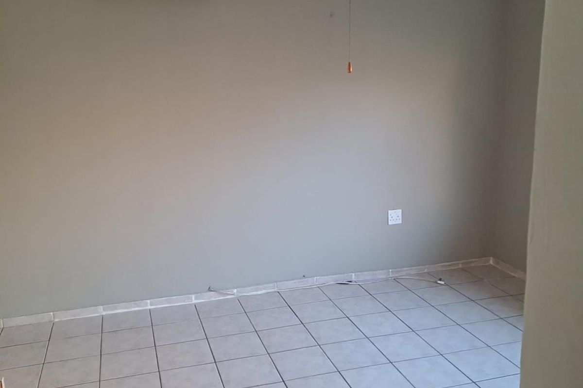 An empty bedroom featuring ceramic tiled flooring, a ceiling fan, and a wall-mounted split-system air conditioning unit.