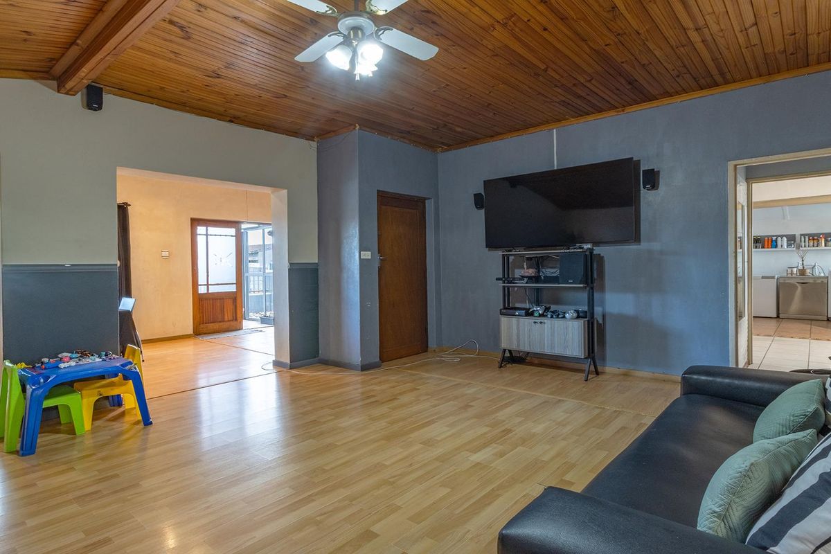 Spacious living room featuring a warm timber-clad ceiling, ceiling fan, and laminate flooring, with open flow to adjacent living areas.