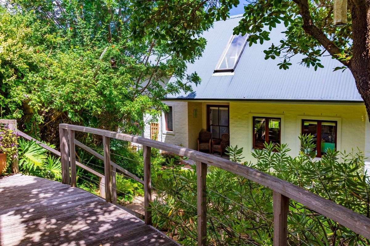 A charming rear exterior view featuring a timber deck, lush garden surroundings, and a pitched roof with a skylight.