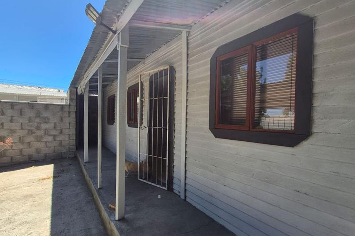 Rear exterior view of the property featuring a covered concrete patio, corrugated metal roofing, and a secure boundary wall.