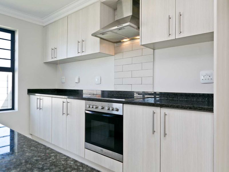 Modern kitchen featuring light wood-grain cabinetry, dark granite countertops, a subway tile backsplash, and integrated stainless steel oven and extractor fan.