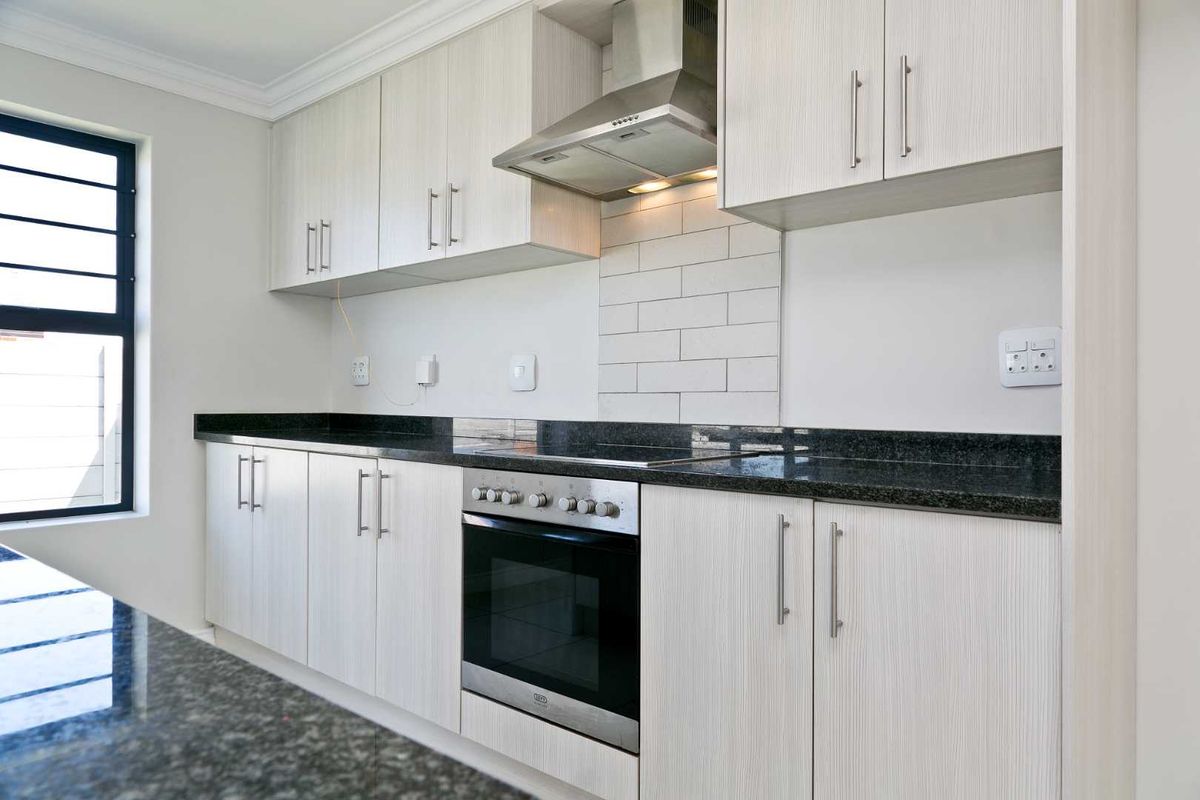 Modern kitchen featuring light wood-grain cabinetry, dark granite countertops, a subway tile backsplash, and integrated stainless steel oven and extractor fan.