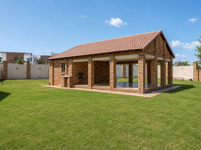 A spacious, covered outdoor entertainment area featuring brick construction, tiled roofing, and a built-in braai, set within a well-maintained garden.