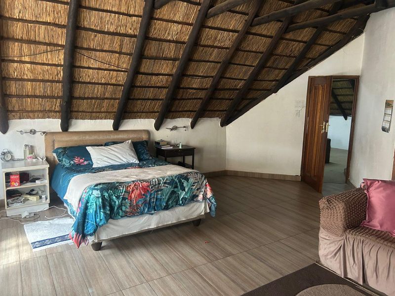 Spacious bedroom featuring a high vaulted thatched roof with exposed timber beams and tiled flooring.