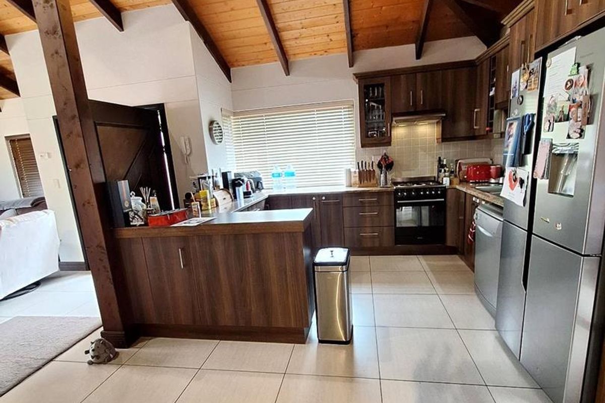 Modern kitchen featuring dark wood cabinetry, tiled flooring, and a vaulted timber ceiling with exposed beams, creating an open and spacious atmosphere.