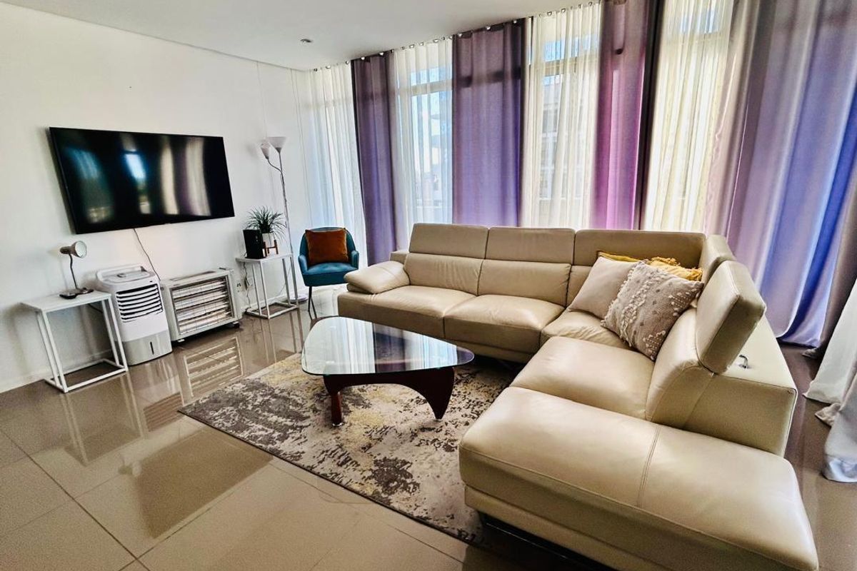A bright and spacious living room featuring large floor-to-ceiling windows with layered curtains and polished tile flooring.