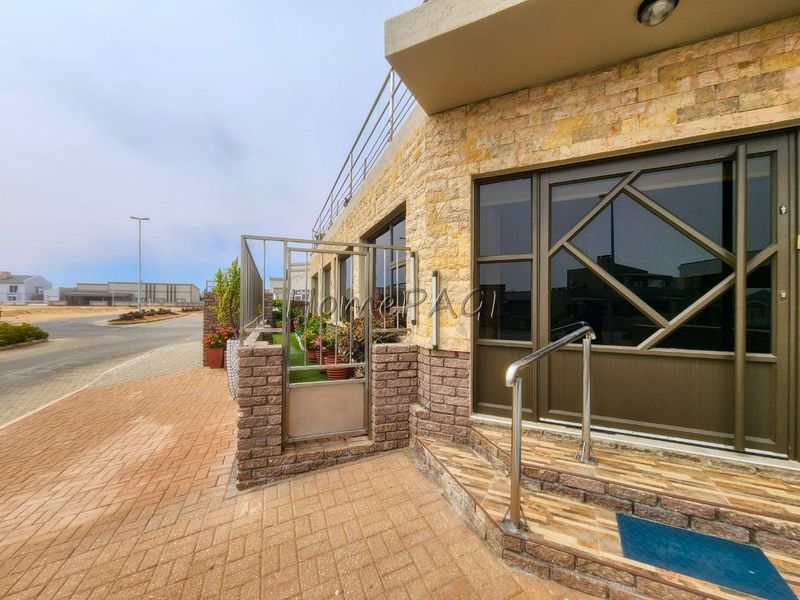 Front entrance area featuring stone cladding, brick paving, and a secure metal gate with a stainless steel handrail leading to the main door.