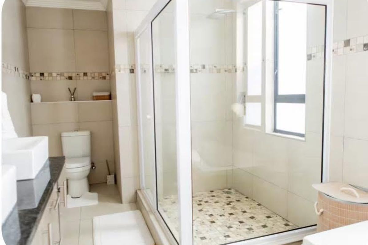 A modern bathroom featuring a glass-enclosed shower, built-in vanity, and neutral wall tiling with decorative mosaic accents.