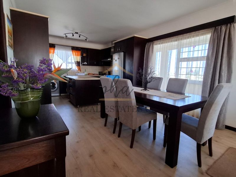 Open-plan living and dining area featuring laminate flooring and a functional kitchen with built-in cabinetry and a central island.