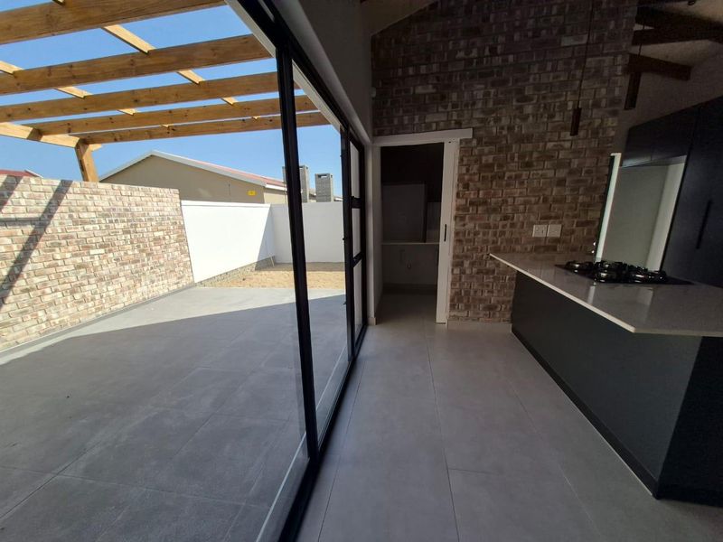 Modern open-plan kitchen area featuring exposed brickwork, sleek cabinetry, and seamless transition to a private tiled patio with a wooden pergola.