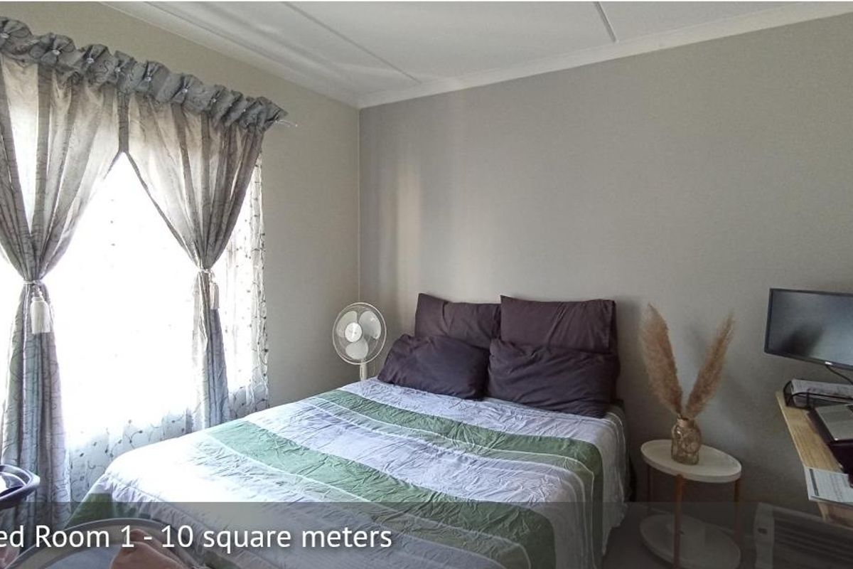 A bedroom featuring neutral wall tones, a large window with curtains, and ample space for a bed and workspace setup.