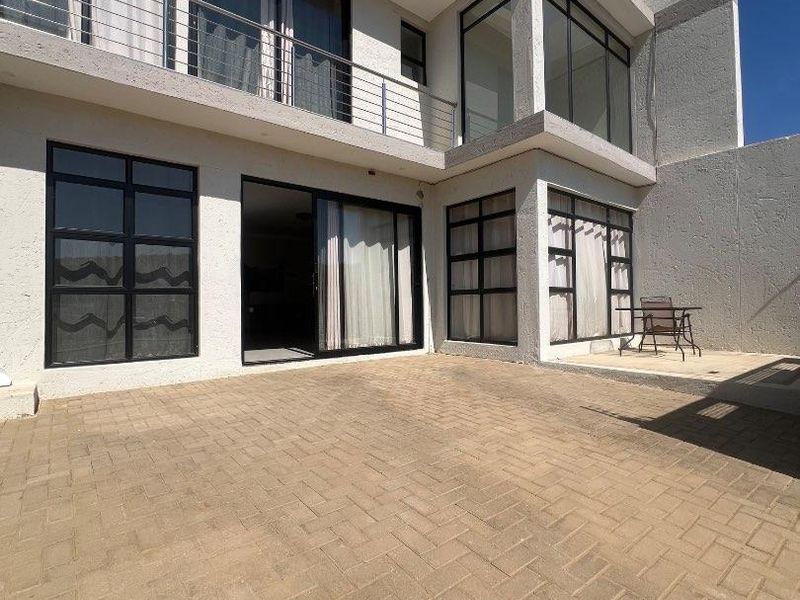 Rear exterior view of a modern townhouse featuring a paved patio area, upper-level balcony, and large sliding glass doors.